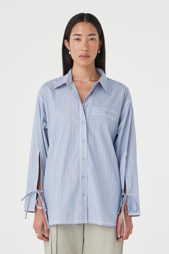 Front view of the Blair Shirt in Blue Taupe Stripe featuring the relaxed silhouette, adjustable waist tie, oversized cuff ties and contrast overlocking, styled with light sage trousers.