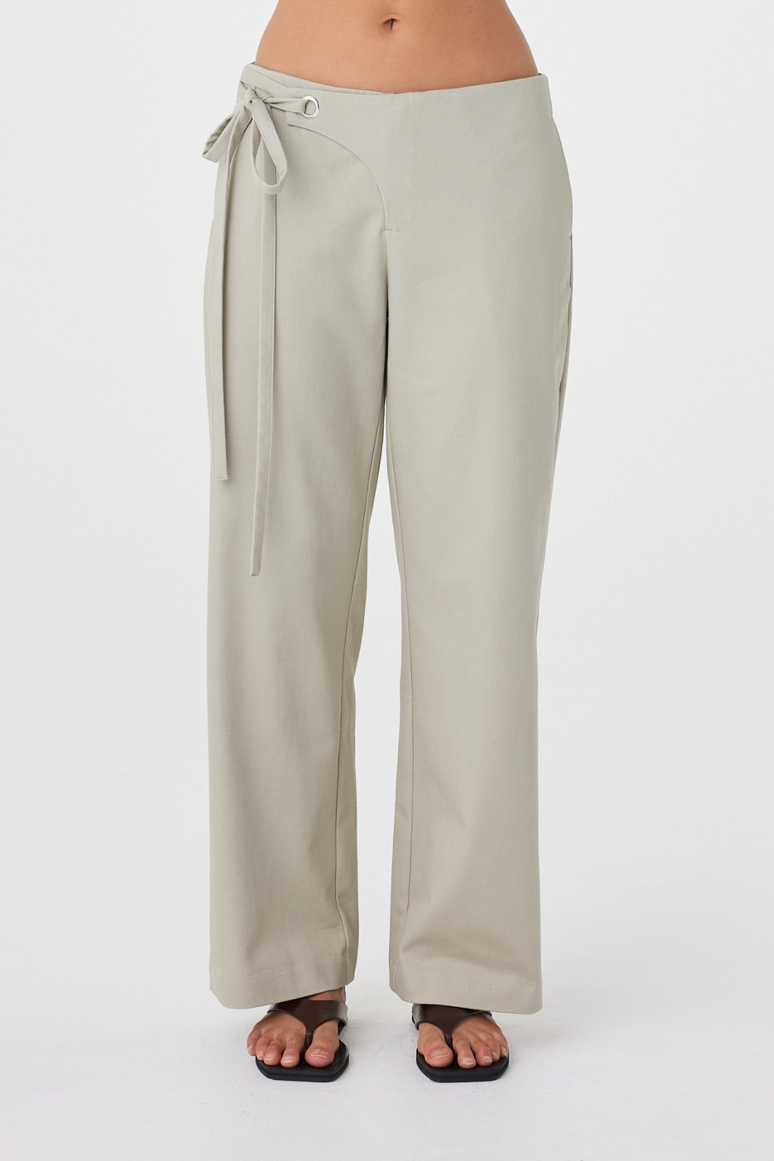 Front detail view of the Lucia Tie Pant in Light Sage showcasing the concealed zip closure, fabric overlap detail and adjustable waist ties.