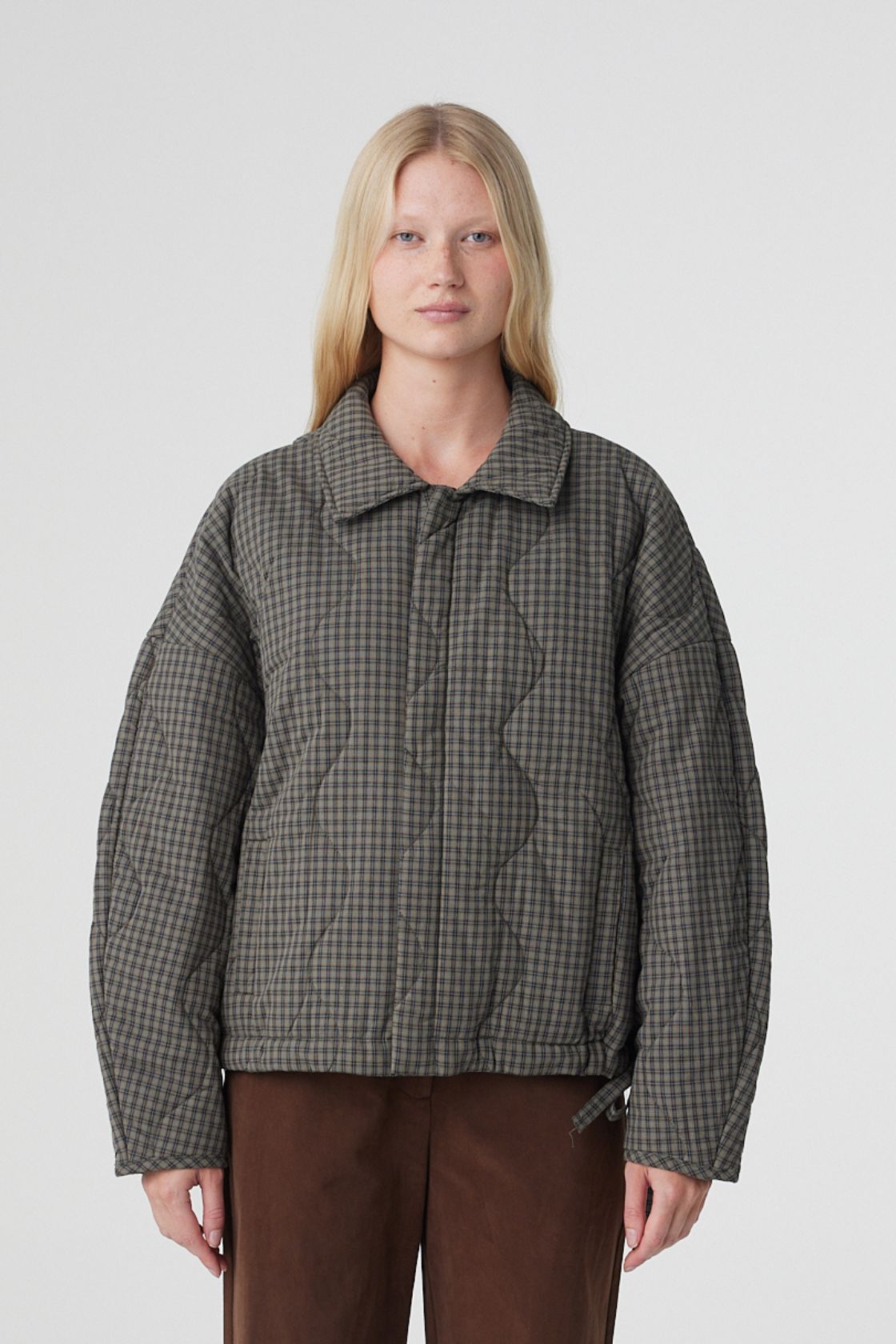 Model wearing the Matteo quilted cotton jacket in olive and teal check, featuring an oversized cocoon silhouette, dropped shoulders, concealed button front and side pockets, styled with espresso pants.