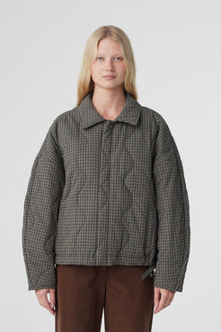 Model wearing the Matteo quilted cotton jacket in olive and teal check, featuring an oversized cocoon silhouette, dropped shoulders, concealed button front and side pockets, styled with espresso pants.