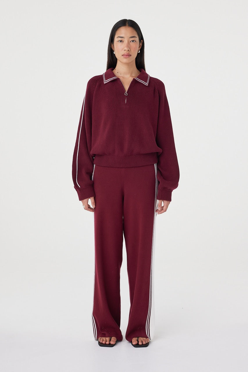 Emery Pant in merlot with cream side stripes, styled with the matching zip-front track top and black sandals, featuring a relaxed straight-leg silhouette and soft drape through the leg