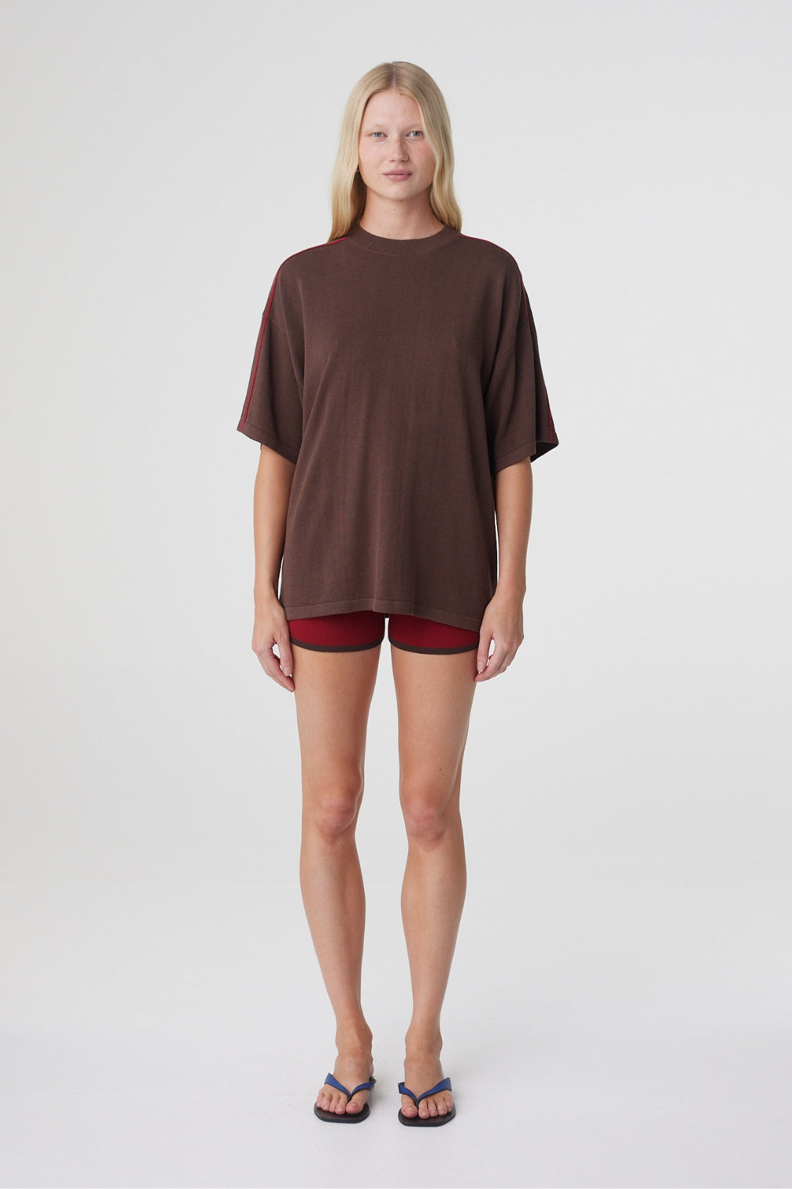 Tove Short in Chilli, full front view styled with an oversized espresso tee, showing the fitted mini silhouette and asymmetric waistband.
