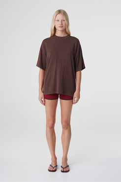 Tove Short in Chilli, full front view styled with an oversized espresso tee, showing the fitted mini silhouette and asymmetric waistband.