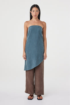 Front view of the Rhea Dress in Teal styled over espresso pants, highlighting the strapless neckline and sweeping asymmetrical hem.