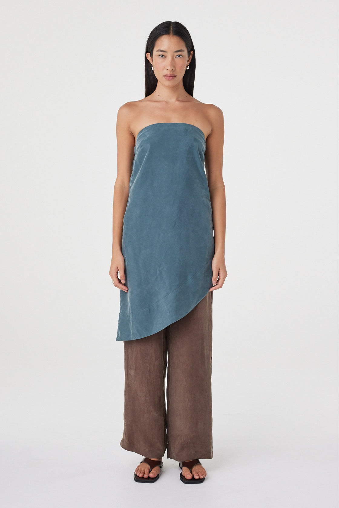 Front view of the Rhea Dress in Teal styled over espresso pants, highlighting the strapless neckline and sweeping asymmetrical hem.