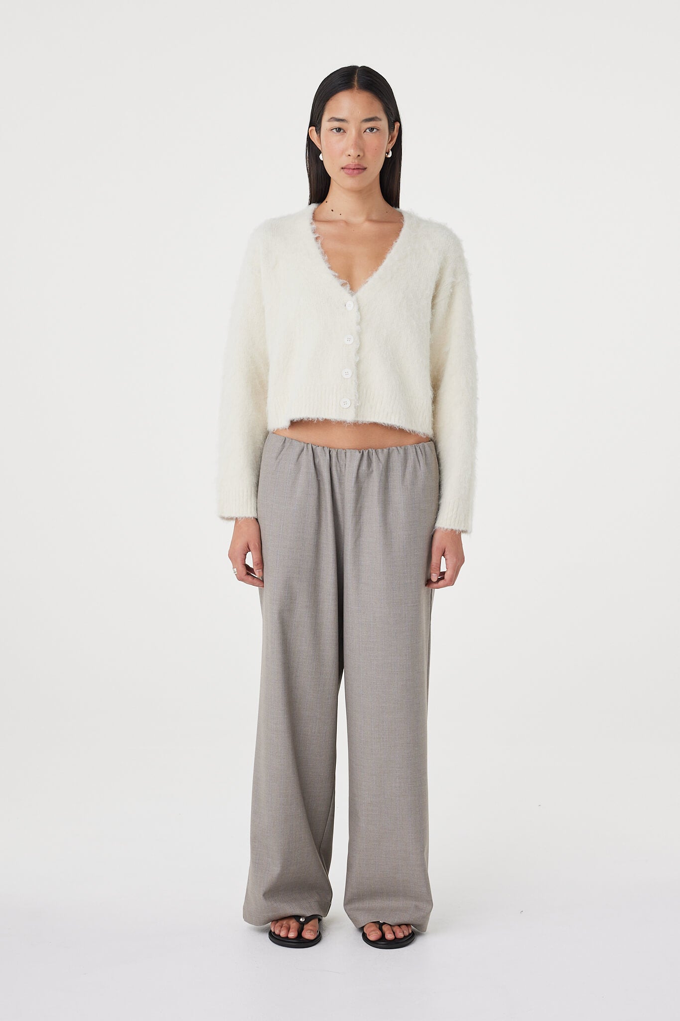 Full-length front view of the Liora Fluffy Cardigan in cream styled with relaxed taupe pants, featuring a button-up front, deep neckline and easy oversized drape