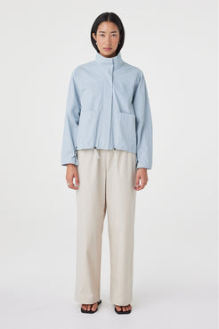 Full-length front view of the Addie Jacket in Pale Blue featuring the funnel neckline, front patch pockets and relaxed fit, styled with wide-leg trousers.