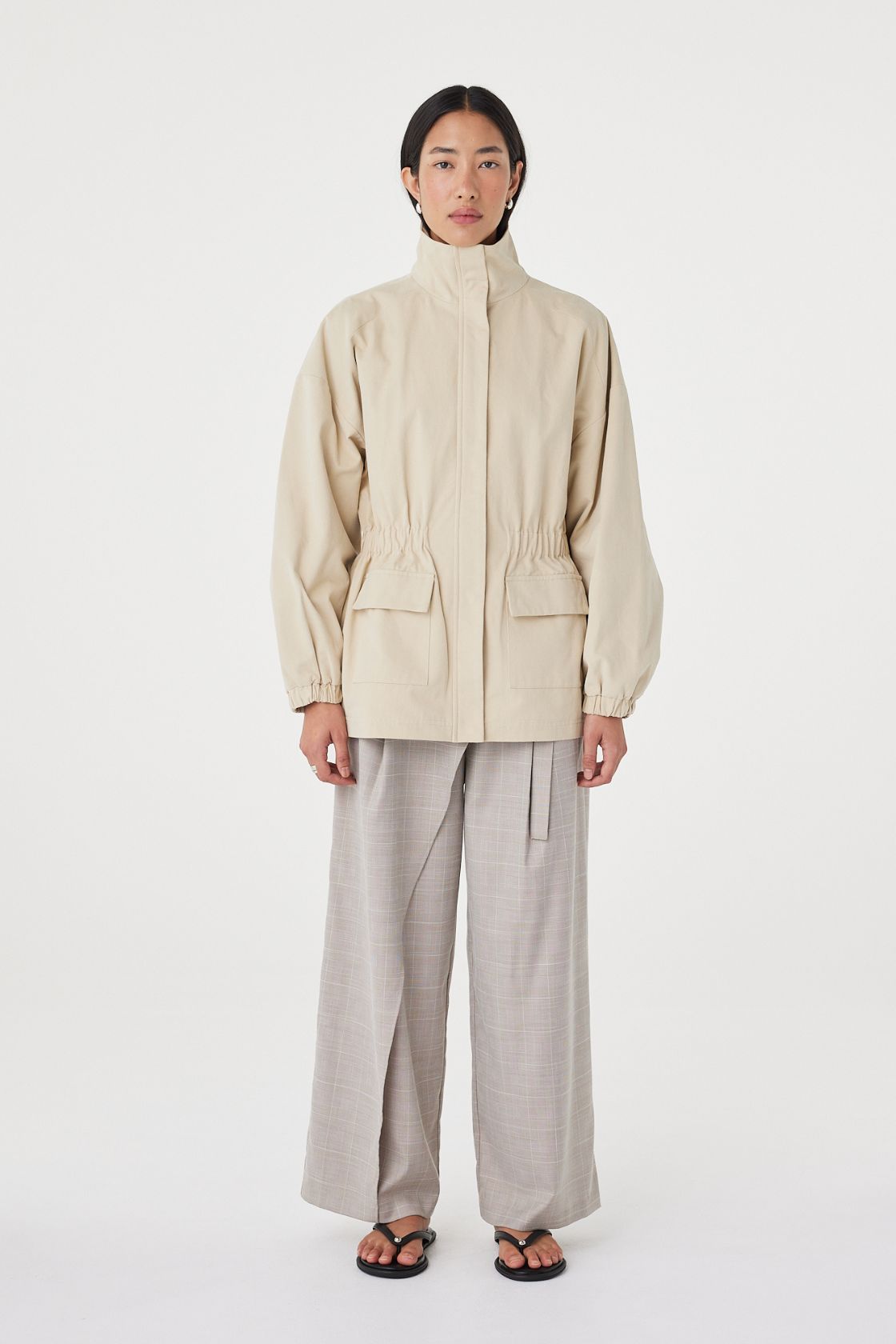 Front view of the Amari Jacket in Beige highlighting the high neckline, patch pockets and gathered waist.
