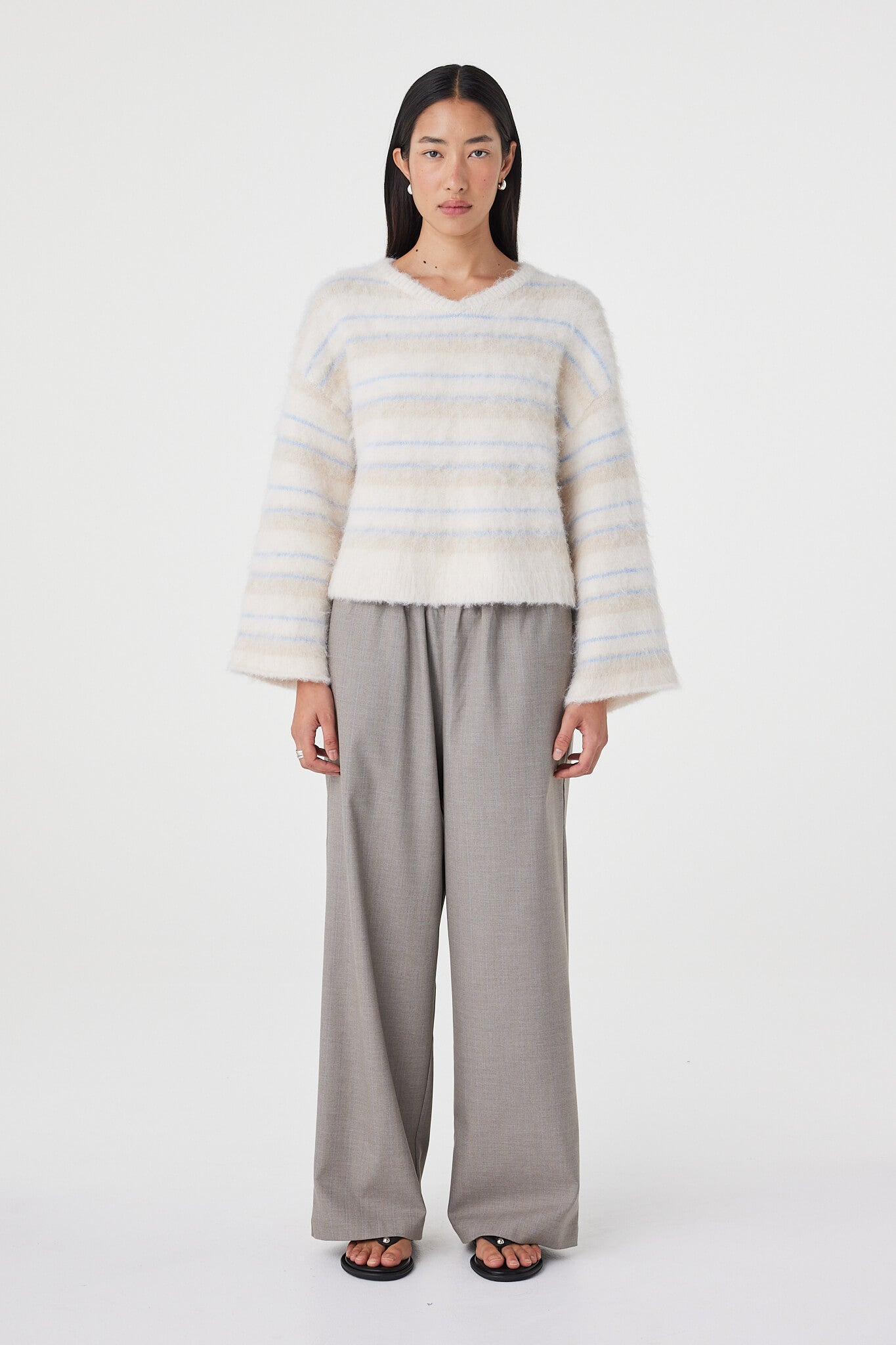 Front view of the Lucca Sweater in taupe and blue stripe featuring a soft fluffy knit texture, relaxed cropped silhouette and deep V-neckline styled with relaxed taupe pants and black sandals
