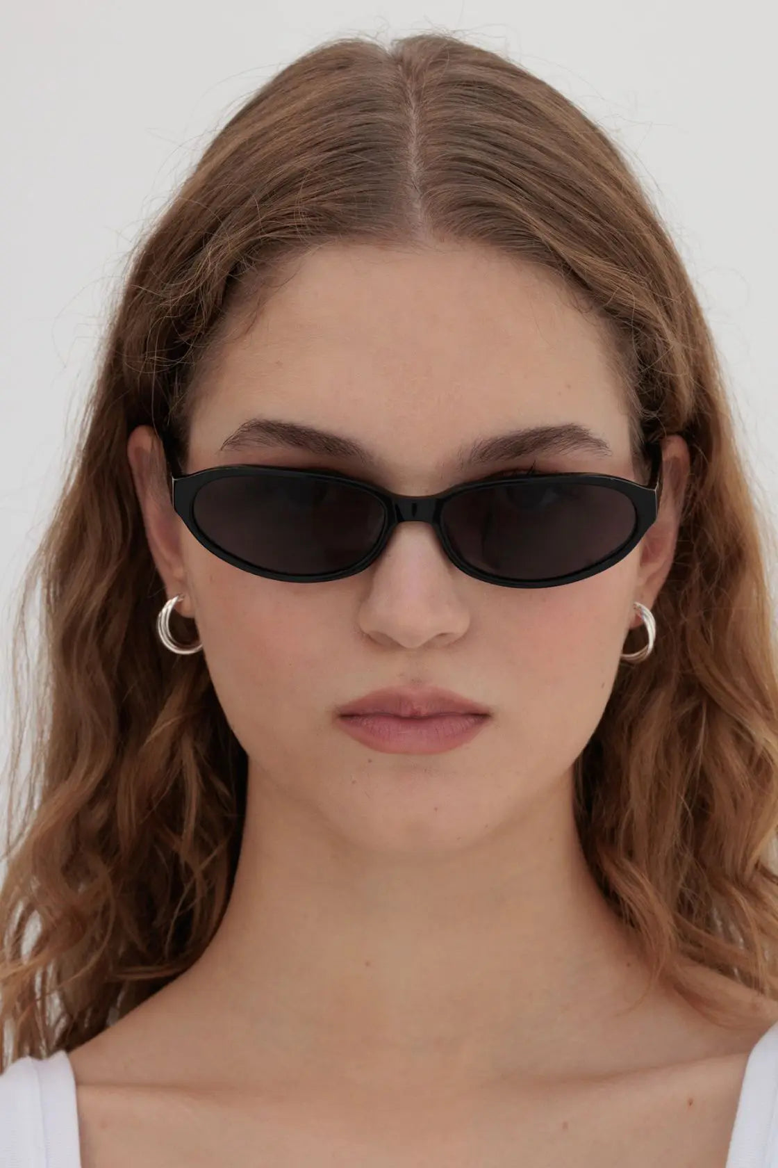 Close-up of black oval sunglasses on model, showing precise fit across the nose bridge and seamless transition into summer styling.
