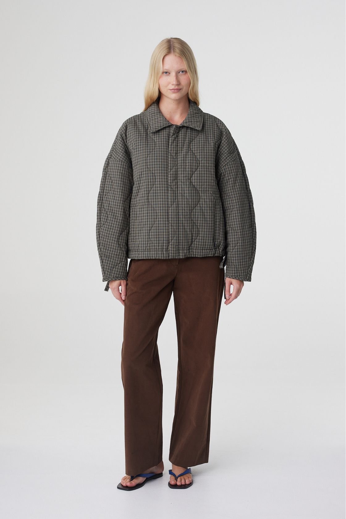 Model wearing the Matteo jacket in olive and teal check styled with espresso pants, highlighting the oversized silhouette, side pockets and quilted texture.