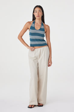 Full-length front view of the Nuri Top in Teal Stripe styled with cream pants, showing the halterneck shape and close fit.