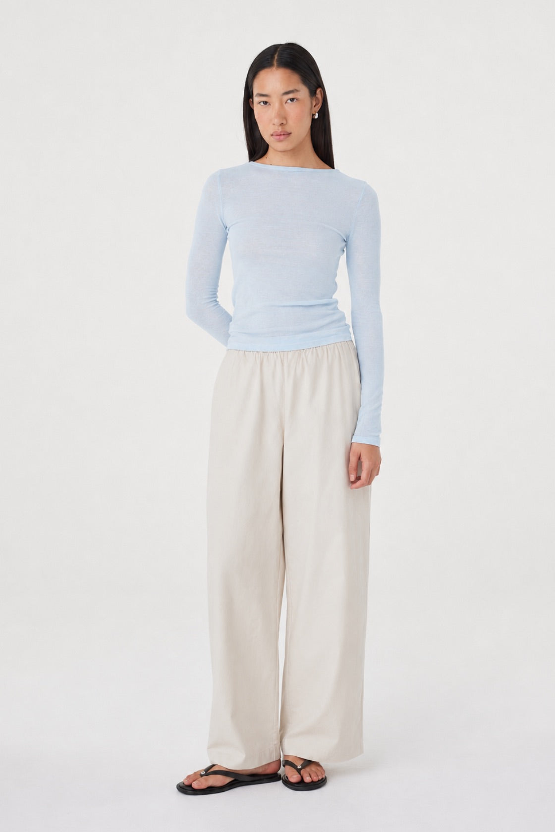 Aston LS Top in Pale Blue styled with the Annika Pants in Taupe, full-length front view with one arm bent, showing the fitted silhouette and soft semi-sheer finish.