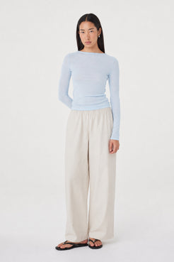 Aston LS Top in Pale Blue styled with the Annika Pants in Taupe, full-length front view with one arm bent, showing the fitted silhouette and soft semi-sheer finish.