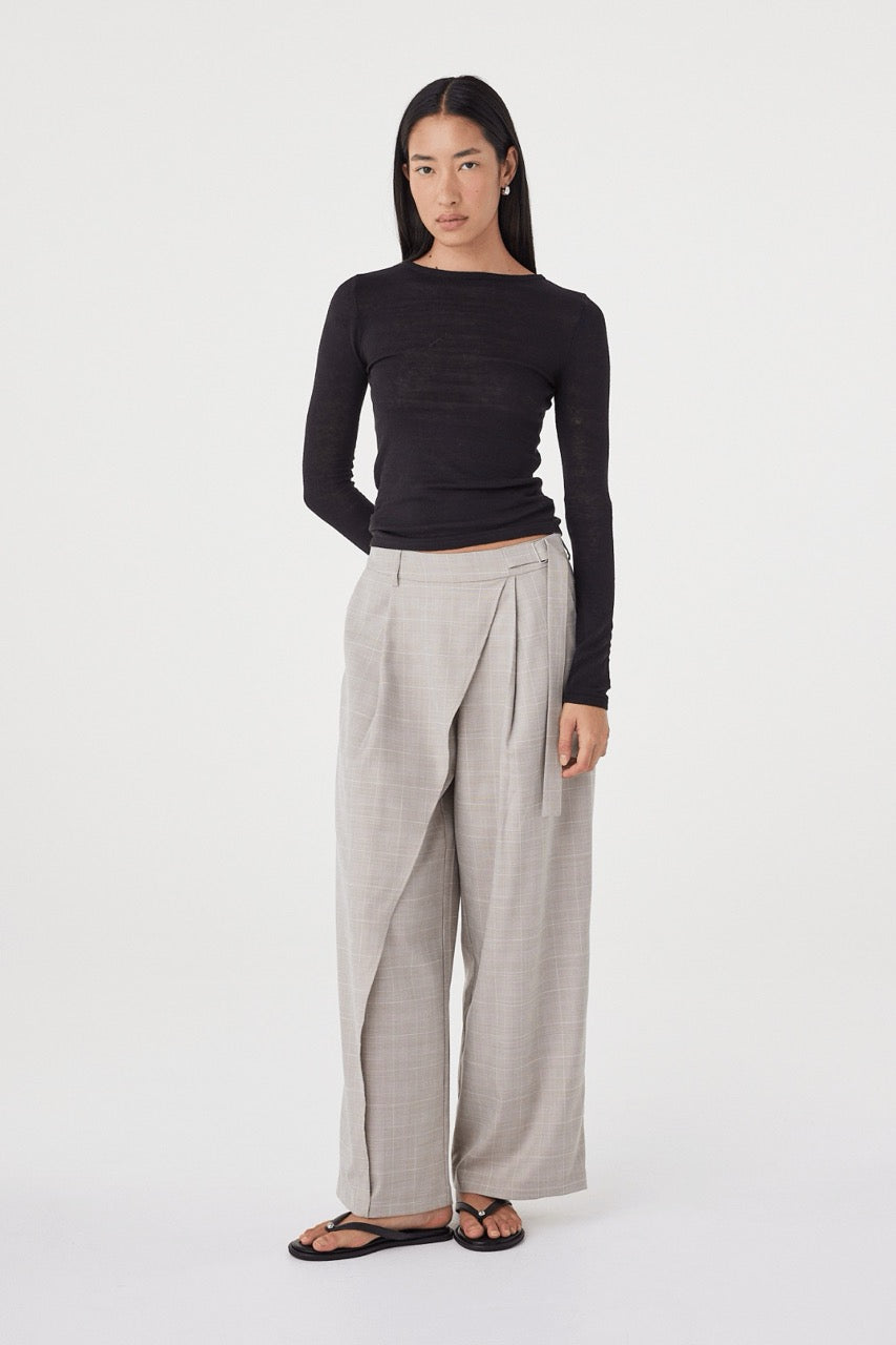 Full-length view of the Aston LS in Black showcasing the slim fit, long sleeves and soft drape through the body, paired with taupe wide-leg trousers and sandals.