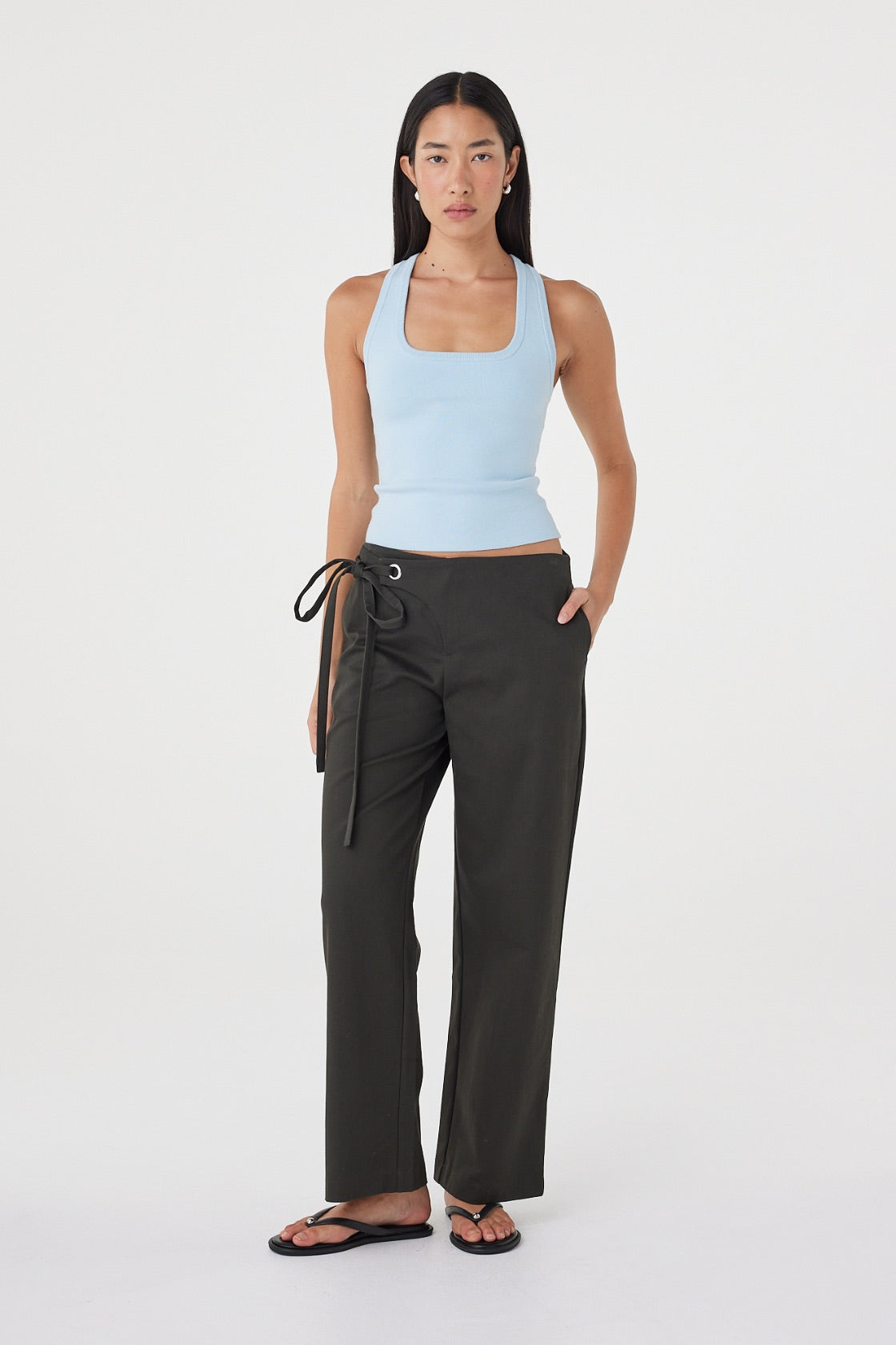 Angled view of the Sable Top in Pale Blue showcasing the square neckline, soft stretch fabrication and fitted shape, paired with charcoal wrap trousers and sandals.