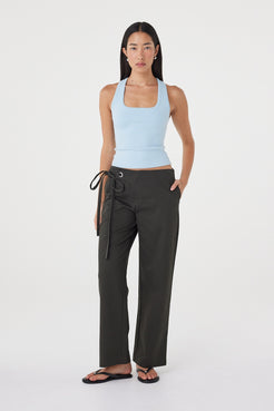 Angled view of the Sable Top in Pale Blue showcasing the square neckline, soft stretch fabrication and fitted shape, paired with charcoal wrap trousers and sandals.