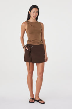 Full-length styled view of the Mable Tank in Deep Cedar showing the streamlined fit and asymmetric shoulder detail, paired with an espresso mini skirt.