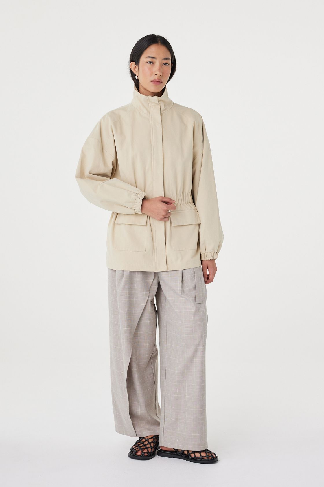 Three-quarter front view of the Amari Jacket in Beige showcasing the gathered waist detail, concealed fastening and utility-inspired design.