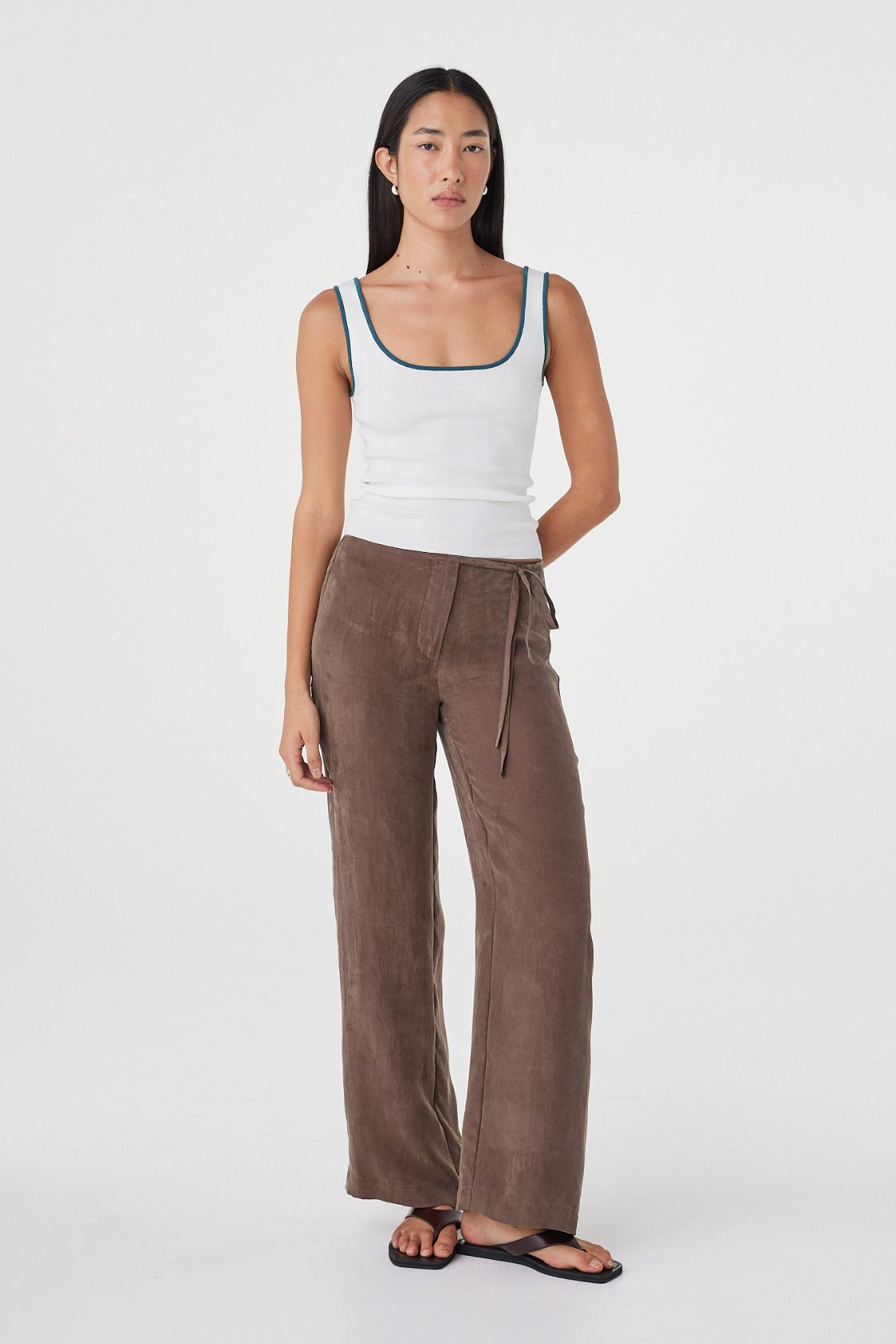 Full-length front view of the Kaya Tank in Cream & Teal showcasing the fitted silhouette and contrast neckline and straps, paired with relaxed brown pants.