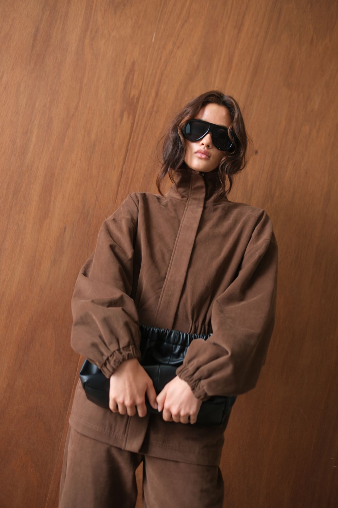 Close-up of the Amari Jacket in Espresso, featuring a structured high neckline, concealed front closure, elasticated cuffs and a softly gathered waist, styled with matching tailored separates and oversized sunglasses.