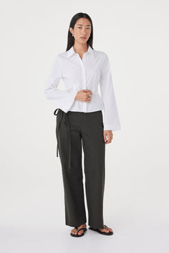 Full-length view of the Ari Shirt in  White showcasing the tailored fit, lightweight cotton fabrication and clean front finish, paired with black trousers and sandals.