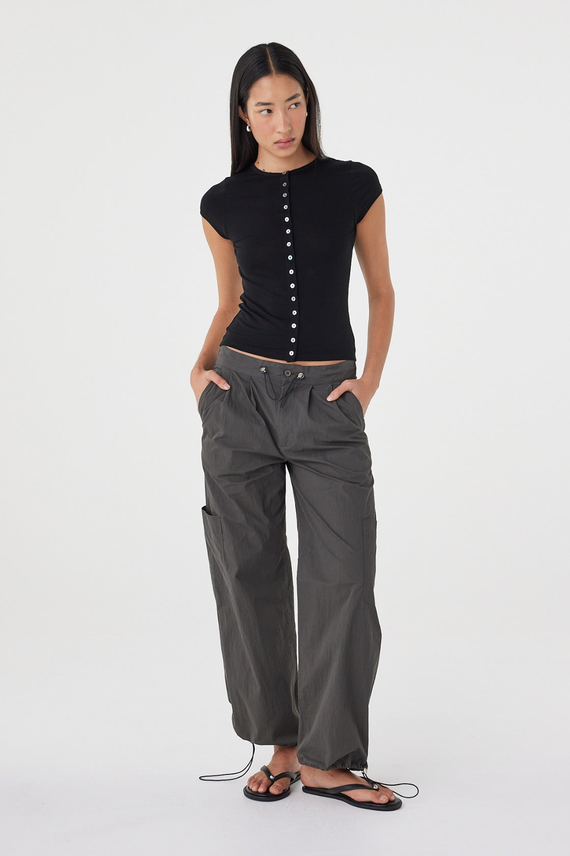 Full-length front view of the Robbie Top in Black showcasing the fitted silhouette, lightweight knit fabrication and cap sleeve design, paired with charcoal utility pants.