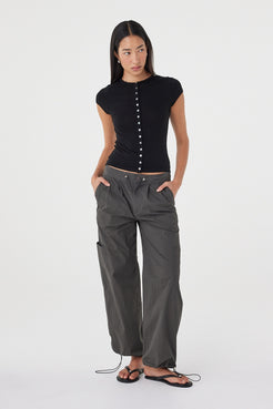 Full-length front view of the Robbie Top in Black showcasing the fitted silhouette, lightweight knit fabrication and cap sleeve design, paired with charcoal utility pants.