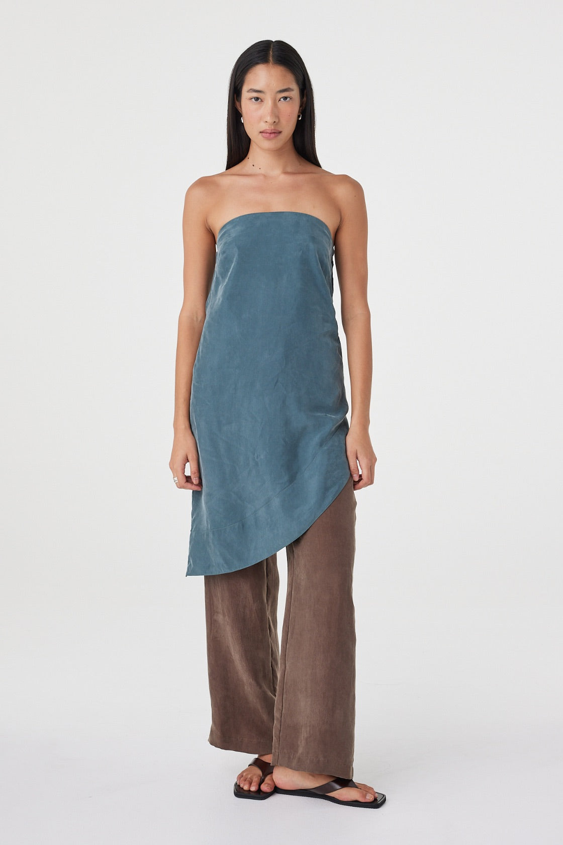 Full-length front view of the Rhea Dress in Teal layered over espresso pants, showing the fluid drape and asymmetrical silhouette.