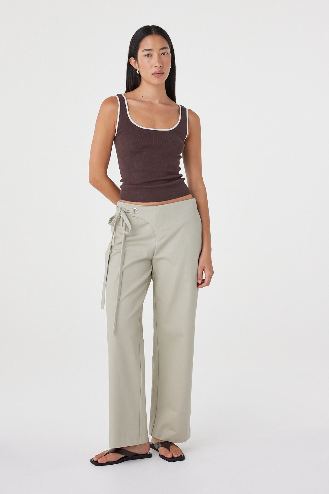 Angled front view of the Lucia Tie Pant in Light Sage styled with a chocolate brown tank, highlighting the relaxed silhouette and utility-inspired waist detailing.