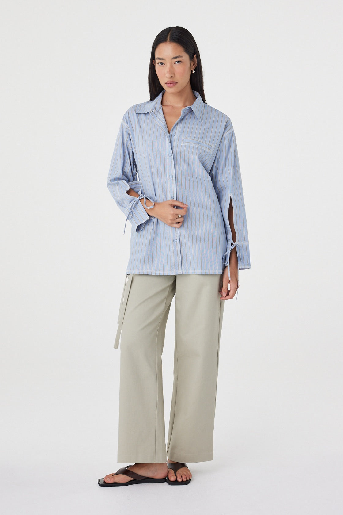 Angled front view of the Blair Shirt in Blue Taupe Stripe showcasing the relaxed fit, vertical stripe pattern and adjustable waist tie, paired with light sage trousers.