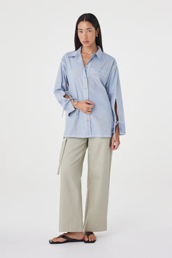Angled front view of the Blair Shirt in Blue Taupe Stripe showcasing the relaxed fit, vertical stripe pattern and adjustable waist tie, paired with light sage trousers.