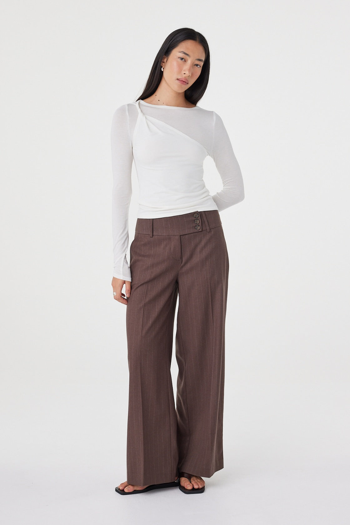Angled front view of the Manon Pant in Espresso Pinstripe styled with a fitted white top, highlighting the tailored waist and effortless drape.