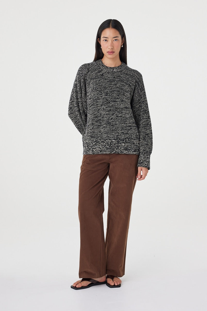 Angled full-length view of the Solene Sweater in black and taupe styled with espresso tailored pants and black sandals for an elevated everyday look