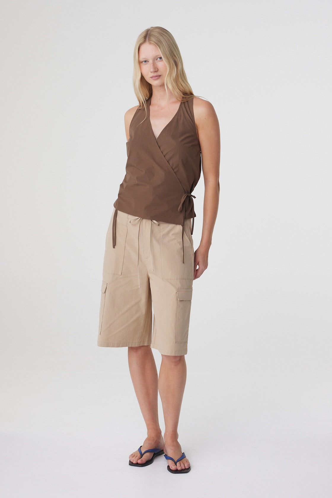 Lilia Wrap Top in Espresso, full length three quarter view styled with beige shorts and flat sandals.