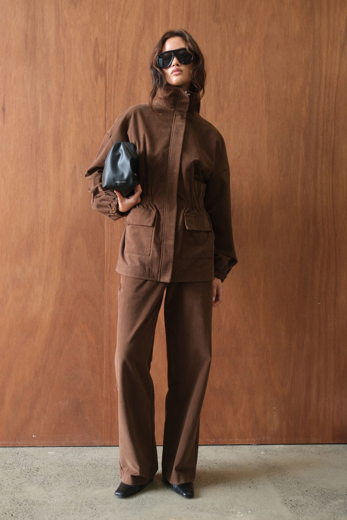 Model wearing the Amari Jacket in Espresso, showcasing the relaxed utility-inspired silhouette, concealed front fastening, patch pockets, gathered waist detailing and high stand collar for a refined, modern finish.