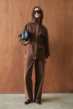 Model wearing the Amari Jacket in Espresso, showcasing the relaxed utility-inspired silhouette, concealed front fastening, patch pockets, gathered waist detailing and high stand collar for a refined, modern finish.