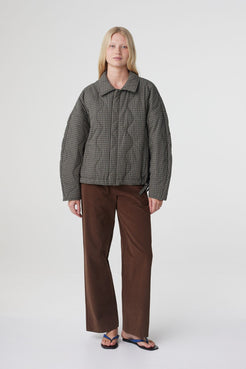 Model wearing the Matteo jacket in olive and teal check with a relaxed oversized fit, elasticated hem and quilted finish, paired with espresso straight-leg pants.