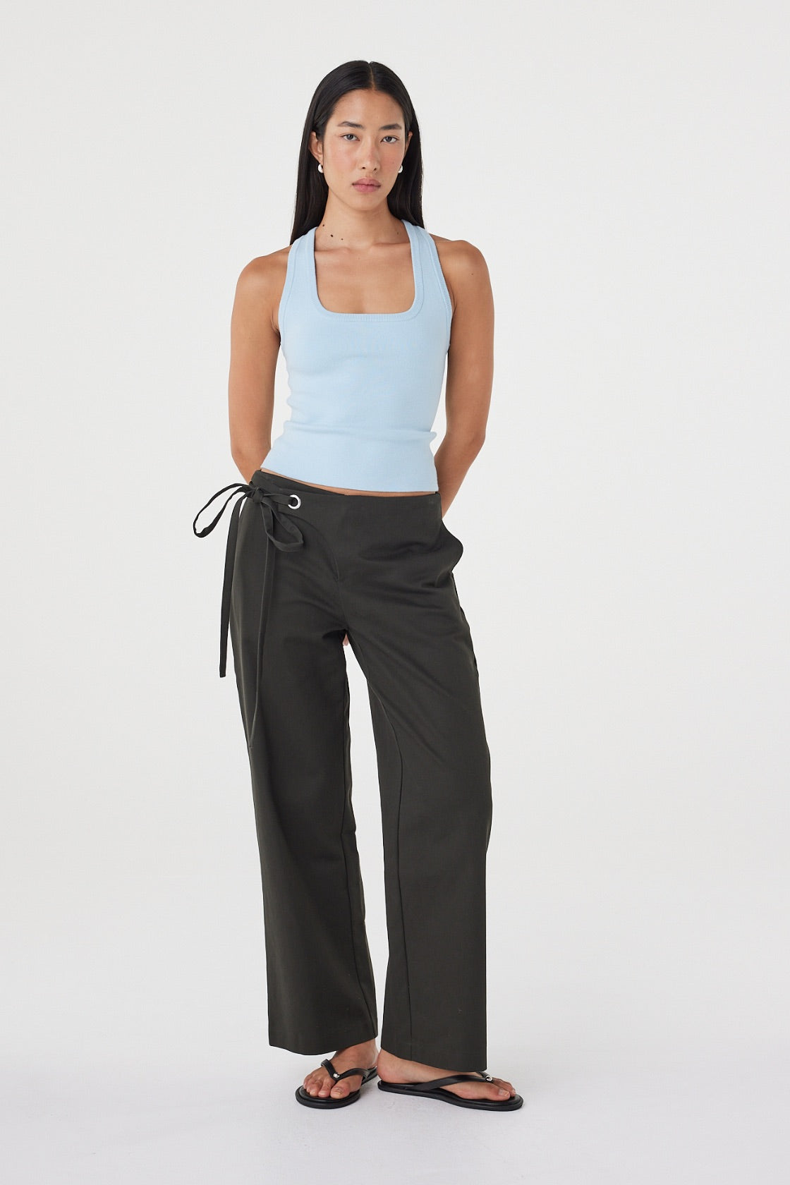 Full-length view of the Sable Top in Pale Blue showcasing the clean fitted shape and smooth finish, paired with charcoal wide-leg wrap trousers and sandals.