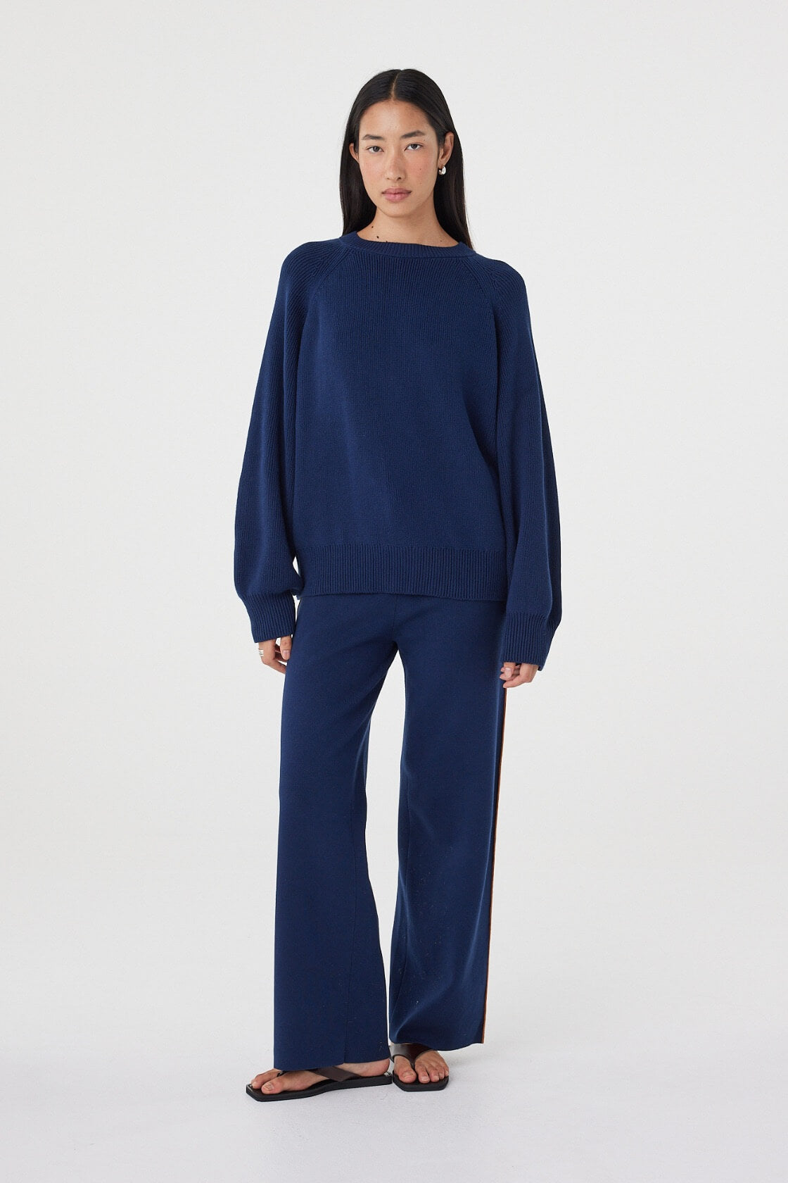 Angled view of the Aubrey Sweater in Navy showcasing the gathered neckline, relaxed fit and lightweight knit texture, styled with matching navy knit pants.