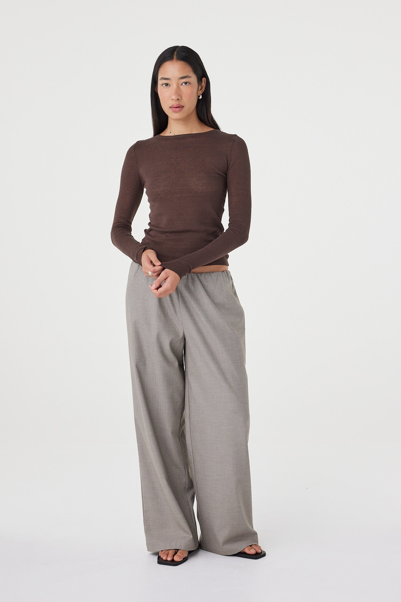 Relaxed full-length view of the Aston LS Top in espresso paired with taupe relaxed pants and black sandals, featuring a fitted silhouette and lightweight cotton-linen knit finish