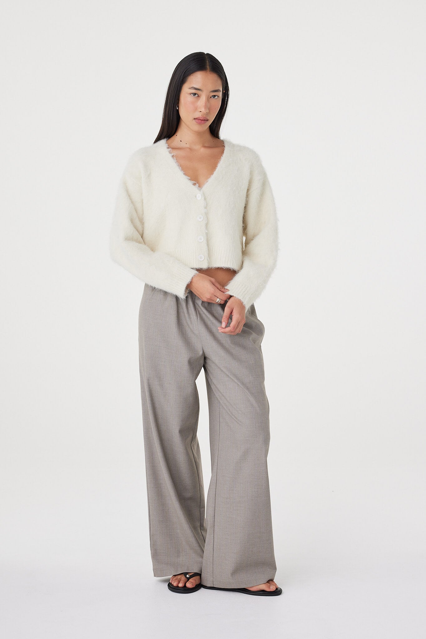 Relaxed front-facing view of the Liora Fluffy Cardigan in cream worn with taupe pants and black sandals, featuring dropped shoulders and a soft cropped silhouette