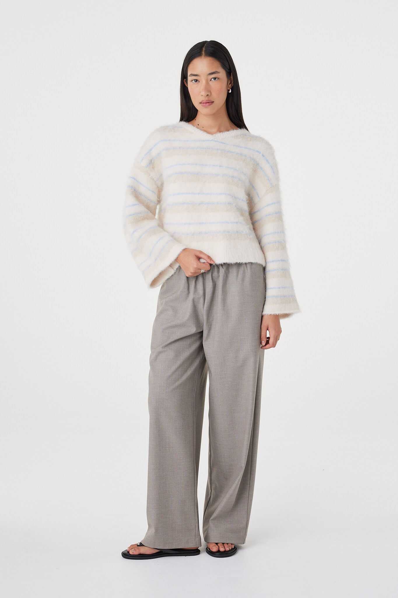 Full-length front view of the Lucca Sweater in taupe and blue stripe styled with wide-leg taupe pants and black sandals, featuring a cropped silhouette and wide sleeve shape

