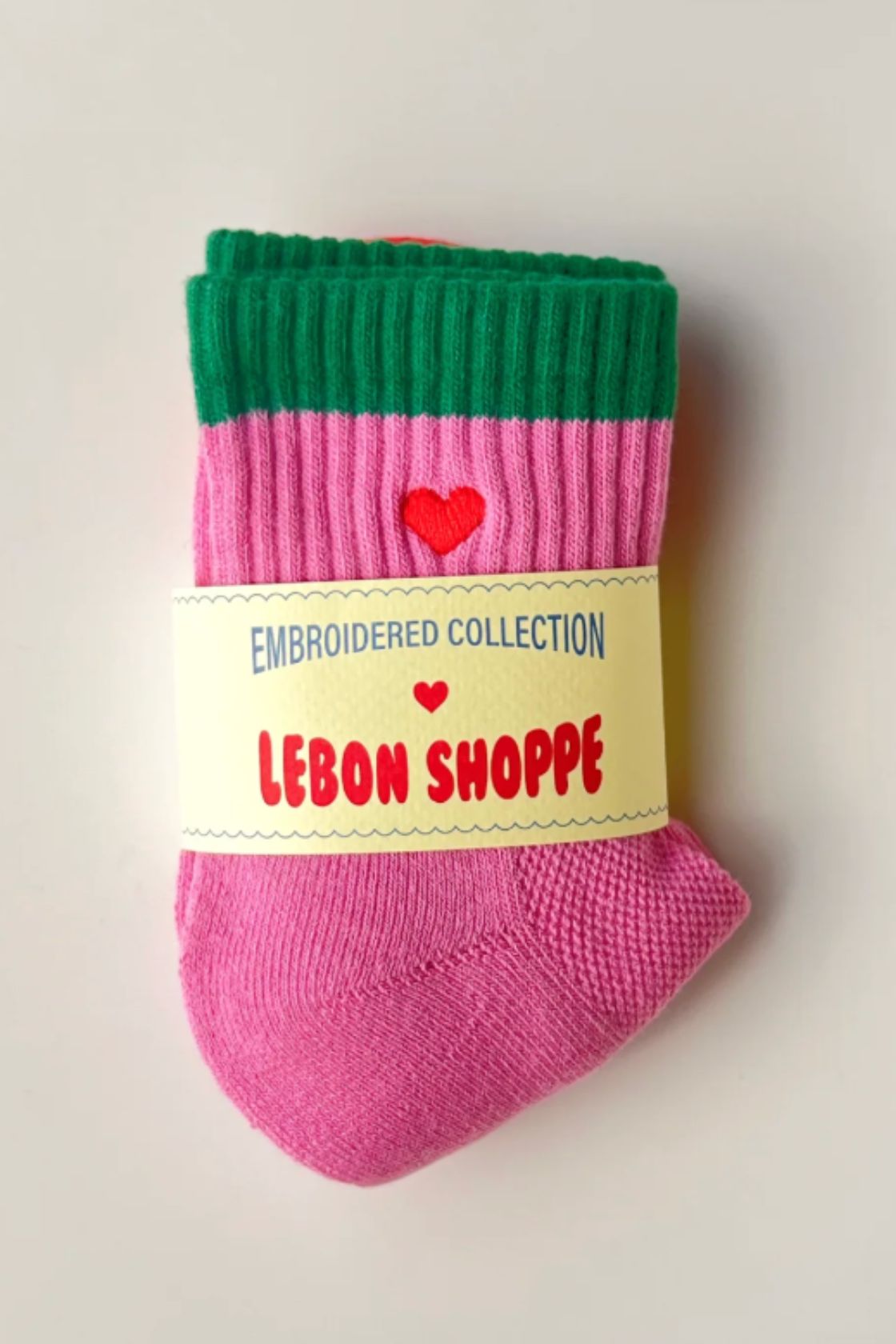 Pink socks with green ribbed cuff and red heart embroidery, folded with Le Bon Shoppe label