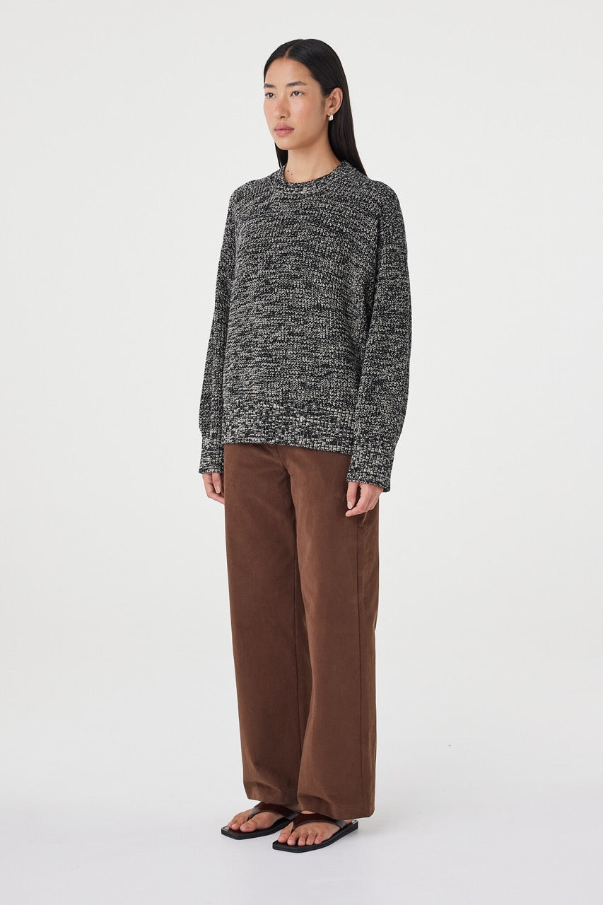 Side profile view of the Solene Sweater in black and taupe paired with espresso straight-leg pants and black sandals, highlighting the soft drape and raglan sleeve shape