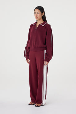 Side profile view of the Nella Zip in merlot and cream styled with relaxed wide-leg knit pants, highlighting the raglan sleeve shape, oversized fit and cream stripe detail down the sleeve