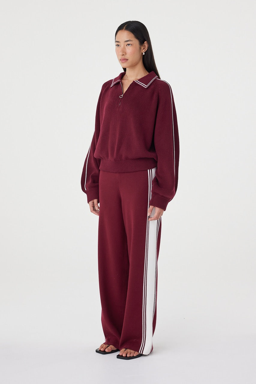 Side profile view of the Nella Zip in merlot and cream styled with relaxed wide-leg knit pants, highlighting the raglan sleeve shape, oversized fit and cream stripe detail down the sleeve