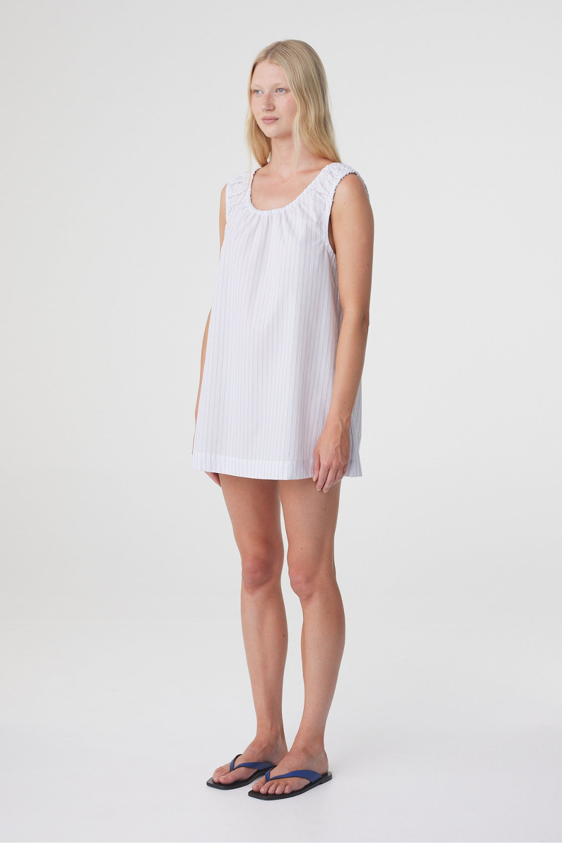 Isla Mini Dress in Blue Pinstripe, three quarter front view highlighting the loose shape, sleeveless cut and mini length.
