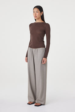 Side profile view of the Aston LS Top in espresso paired with taupe wide-leg pants and black sandals, highlighting the close fit through the body and lightweight drape