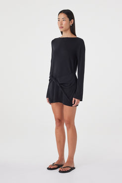 Angled view of the Kira Mini Dress in Black highlighting the clean neckline, relaxed long sleeves and asymmetric drape created by the front twist.